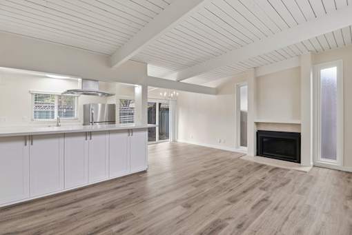 A spacious living room with a fireplace and a kitchen area with white cabinets.