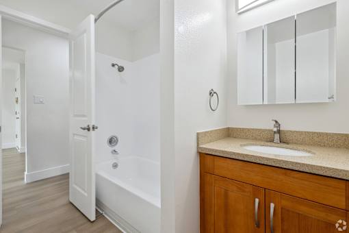 A white bathroom with a sink, mirror, and bathtub.