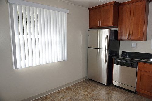 A kitchen with a stainless steel refrigerator and a window with blinds.