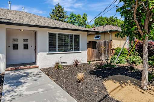 A house with a white door and windows with a small garden in front.