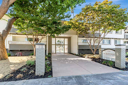 The image shows a building entrance with a sign that reads "meirose" and is surrounded by trees and shrubs.