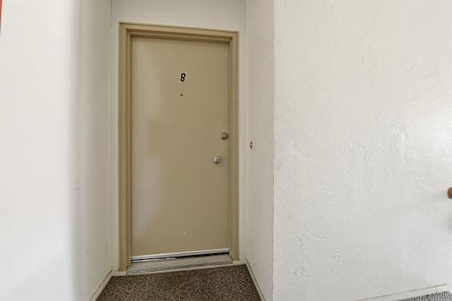 A brown door with a silver handle is in a white room.
