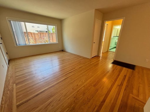 an empty living room with wood floors and a large window
