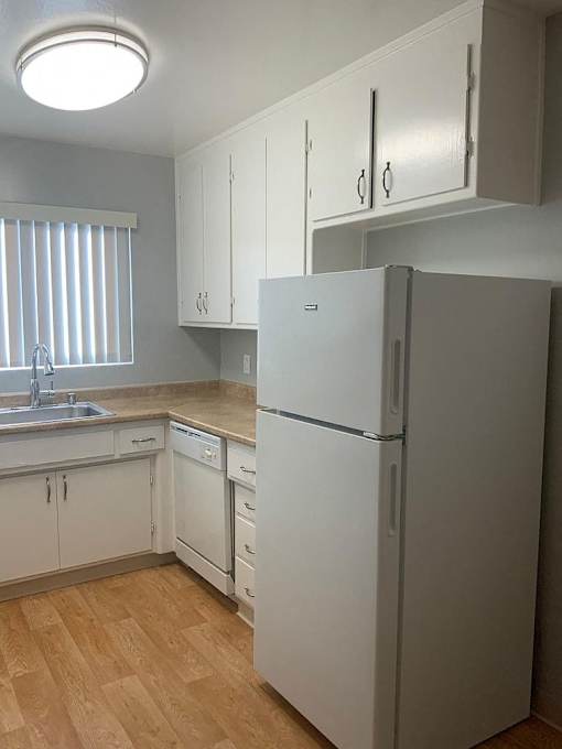 A white refrigerator in a kitchen with wooden floors and white cabinets.