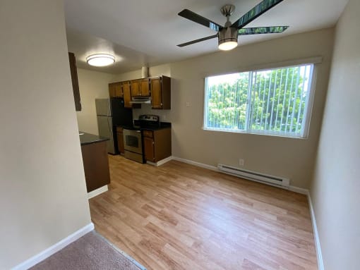 an empty living room with a kitchen and a ceiling fan