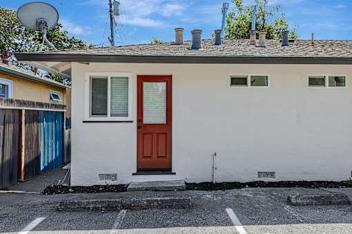 A small white house with a red door is situated on a street.