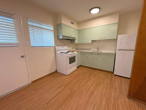 A kitchen with wooden flooring and white appliances.