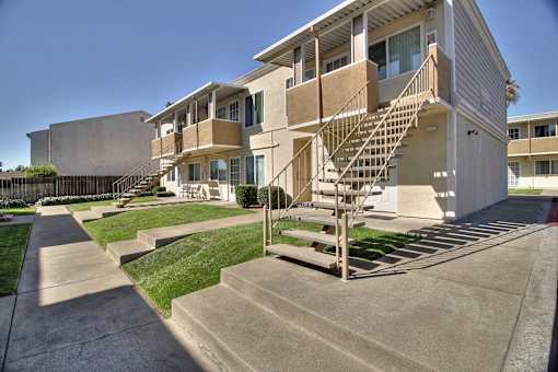 A concrete staircase leads to a balcony on a two-story apartment building.