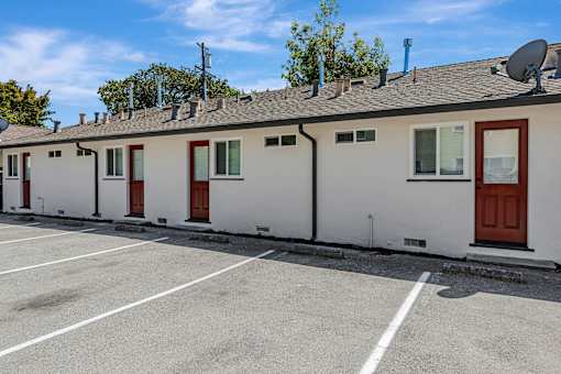 A white building with red doors and windows is under a clear blue sky.