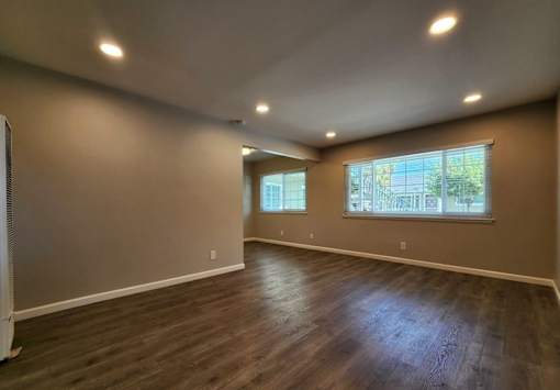 A spacious room with wooden flooring and two windows.