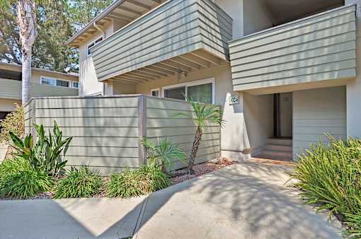 A house with a green fence and plants in front.