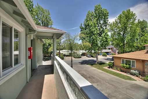 A balcony with a railing overlooks a tree-lined street.