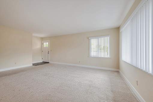 A large empty room with a carpeted floor and a window with blinds.