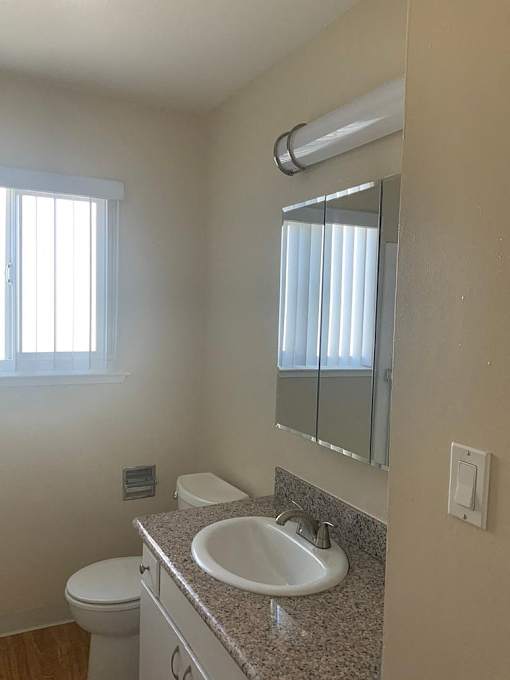 A bathroom with a sink, toilet, mirror, and window.