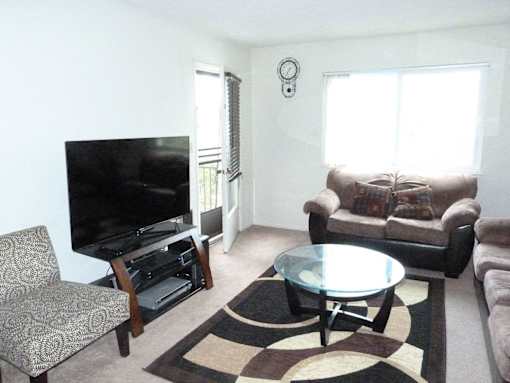 A living room with a flat screen TV and a glass coffee table.