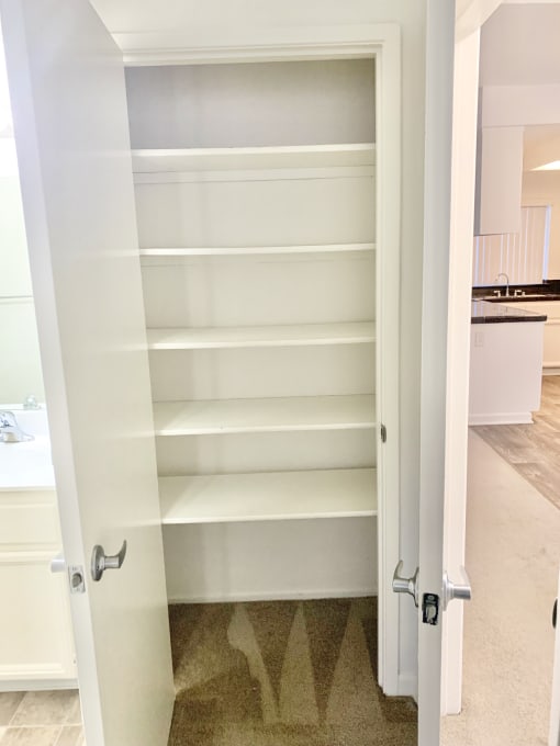 a closet with white shelves and a door open