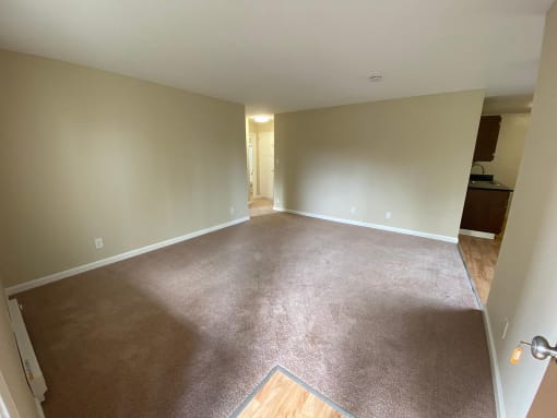 an empty living room with carpet and a kitchen