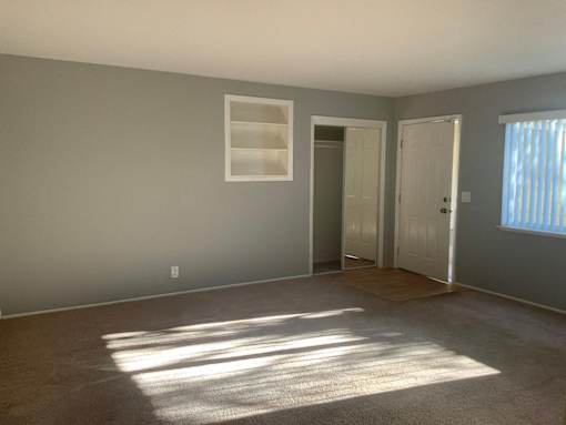 A room with a carpeted floor and a window letting in sunlight.
