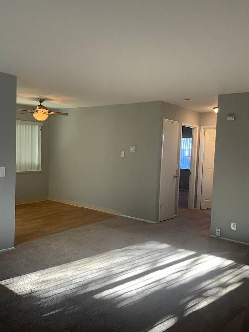 A room with a ceiling fan and a door leading to another room.