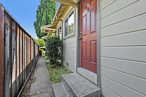 A red door is on the right side of a grey house.