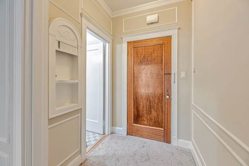 A room with a wooden door and a white wall.