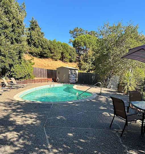 A pool surrounded by trees and a fence with a patio table and chairs.