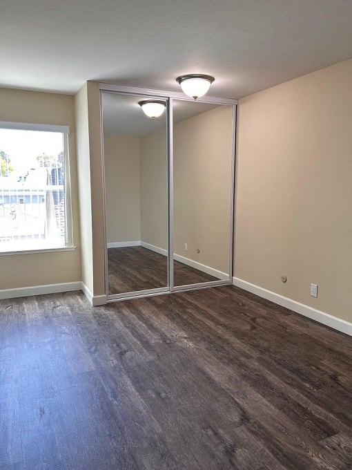 an empty living room with wood floors and a mirrored closet
