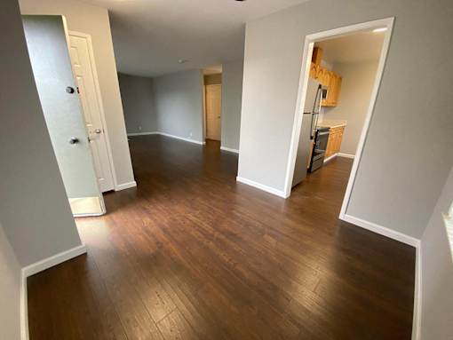 a living room and hallway with wood floors and a kitchen