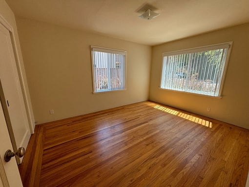 an empty living room with wood floors and two windows