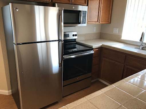 A stainless steel refrigerator stands in a kitchen with wooden cabinets and a black oven.