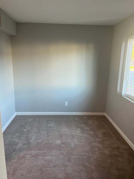an empty room with a carpet and two windows