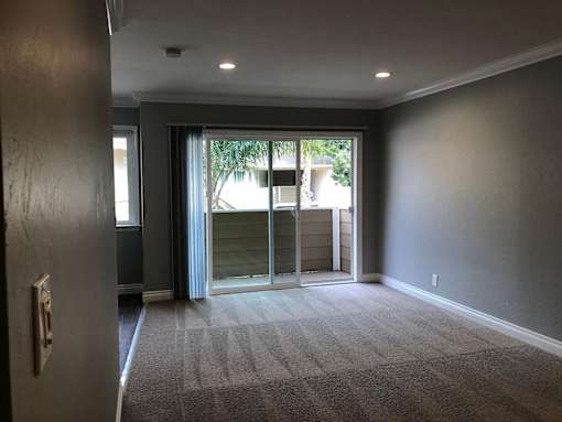 A room with a carpeted floor and a sliding glass door leading outside.