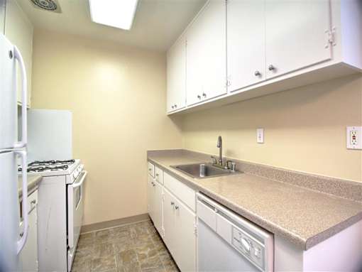 A kitchen with a white refrigerator, a white stove, a white dishwasher, and white cabinets.