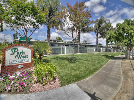A sign for Park West Apartments is in front of a building and trees.
