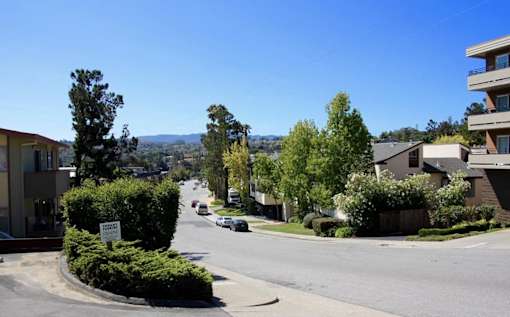 A street view of a residential area with cars parked on the side of the road.