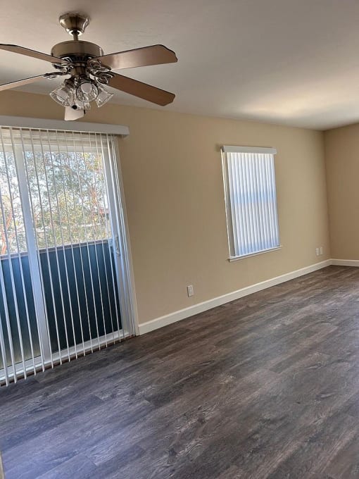 an empty living room with a large window and a ceiling fan