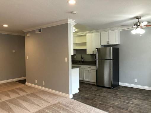 A kitchen with a refrigerator, cabinets, and a ceiling fan.