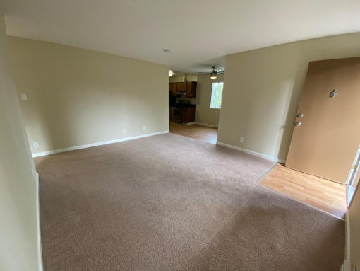 an empty living room with a carpeted floor and an open door to a kitchen