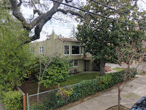 A house with a green fence and a tree in front of it.