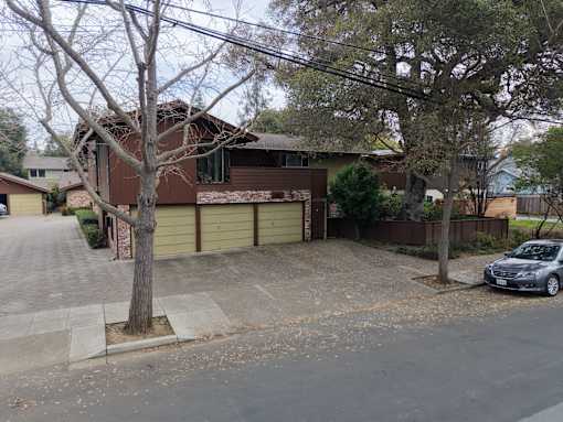 A brown house with a grey car parked in front.