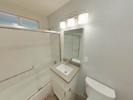 A white bathroom with a sink, mirror, and toilet.