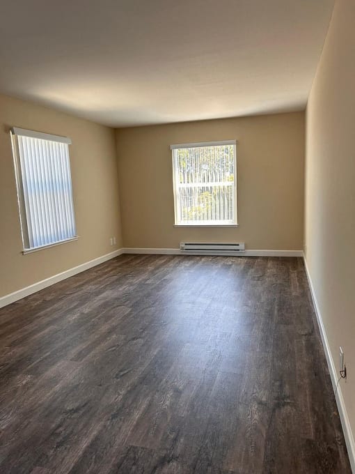 an empty room with wood floors and two windows