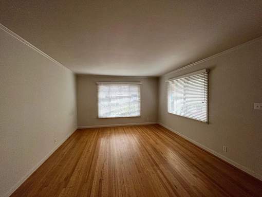 A room with wooden floors and two windows with blinds.