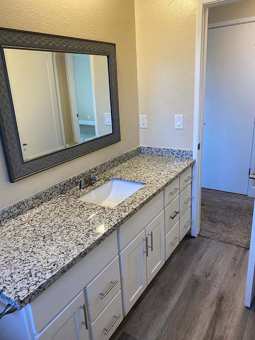 A bathroom with a granite counter top and white cabinets.