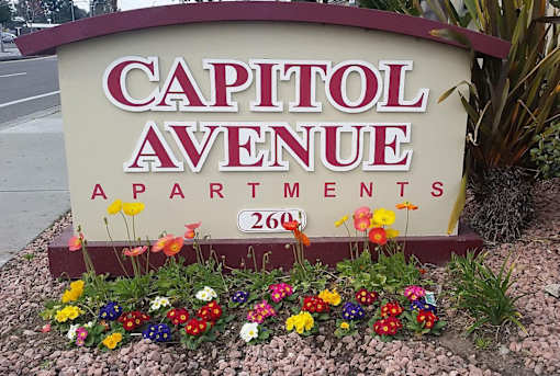 A sign for Capitol Avenue Apartments with flowers in front.