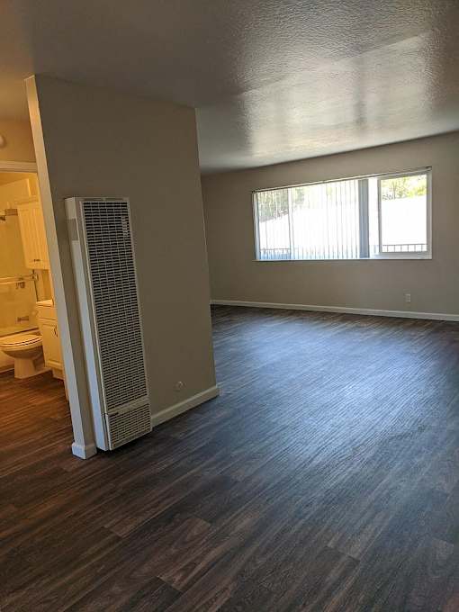 A room with a wood floor and a window with blinds.