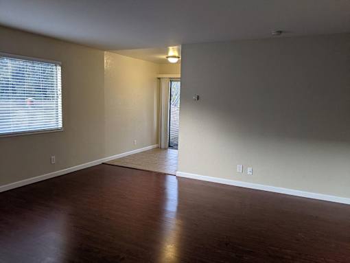 A room with wooden floors and a window with blinds.