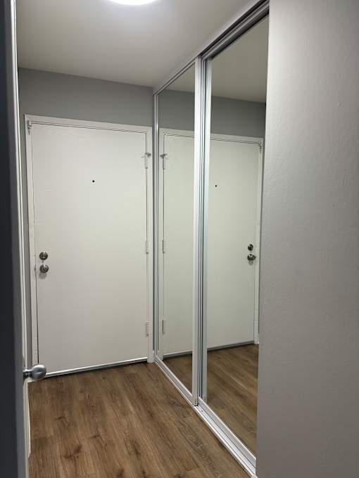 A white cabinet with two doors is open, revealing a wooden shelf inside.