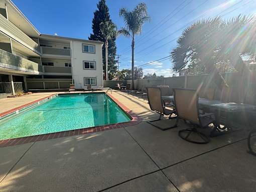 A pool surrounded by chairs and trees in front of a building.