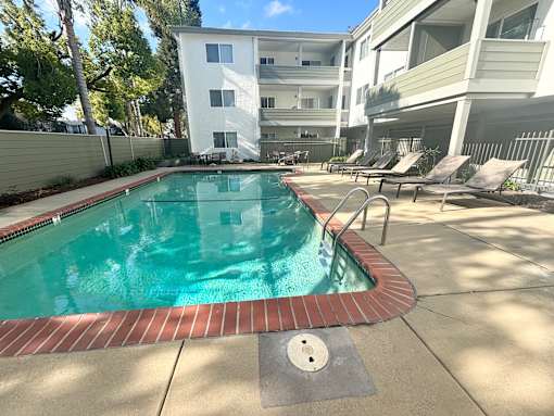 A swimming pool surrounded by a concrete patio and a white apartment building.